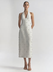 Woman wearing a white dress with embellished details on a plain background