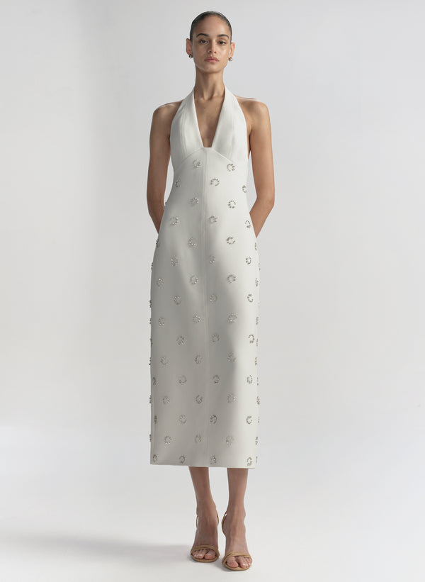 Woman wearing a white dress with embellished details on a plain background