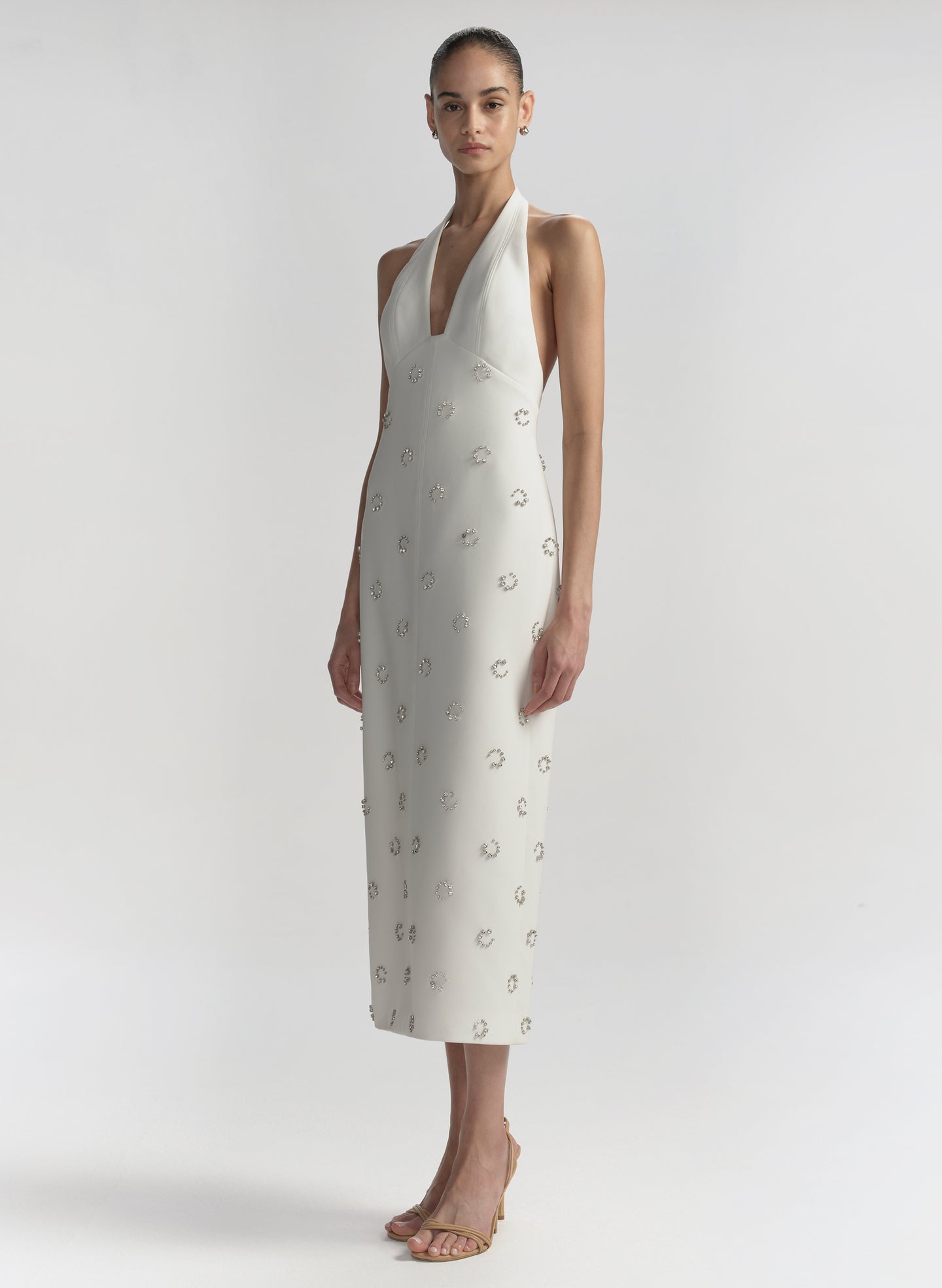 Woman wearing a white dress with embellished details on a plain background