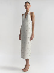 Woman wearing a white dress with embellished details on a plain background