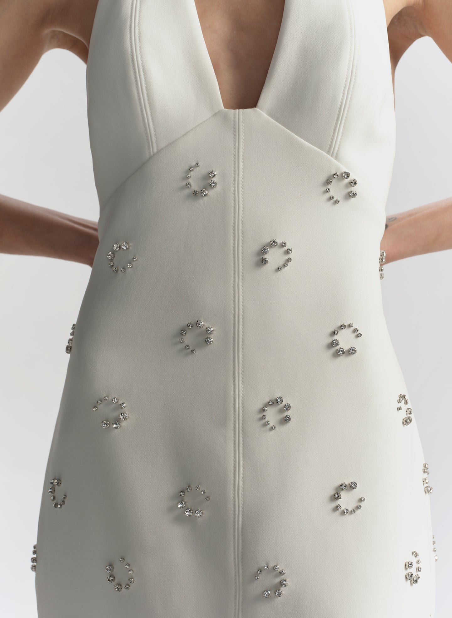 Woman wearing a white dress with embellished details on a plain background