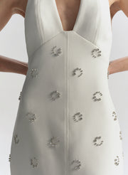 Woman wearing a white dress with embellished details on a plain background