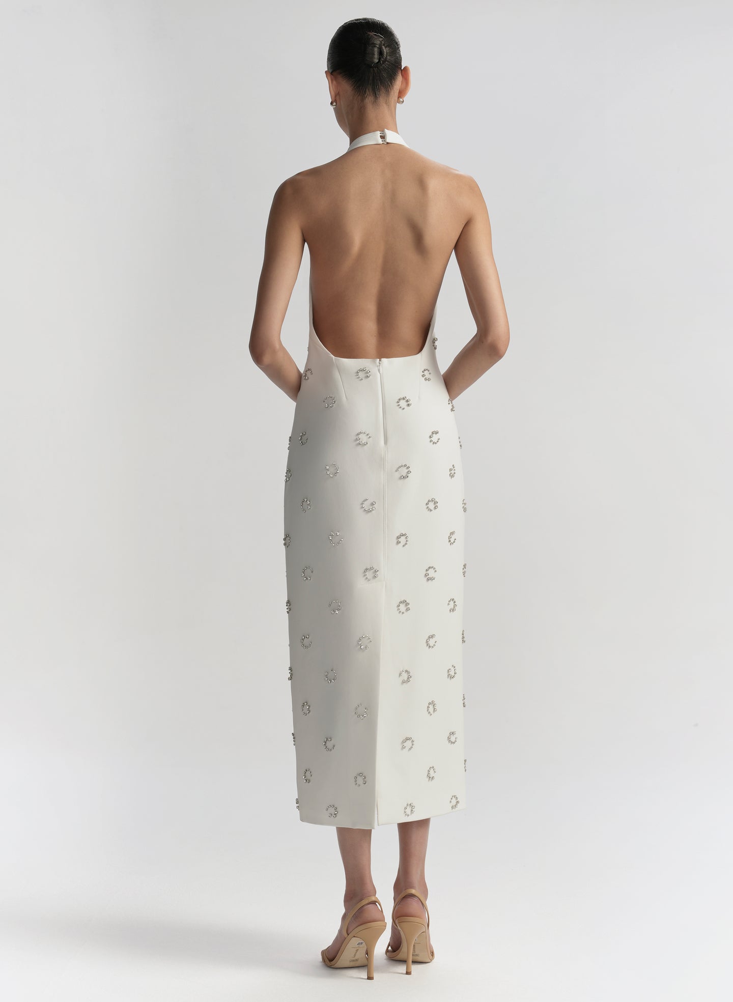 Woman wearing a white dress with embellished details on a plain background