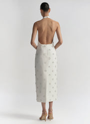 Woman wearing a white dress with embellished details on a plain background