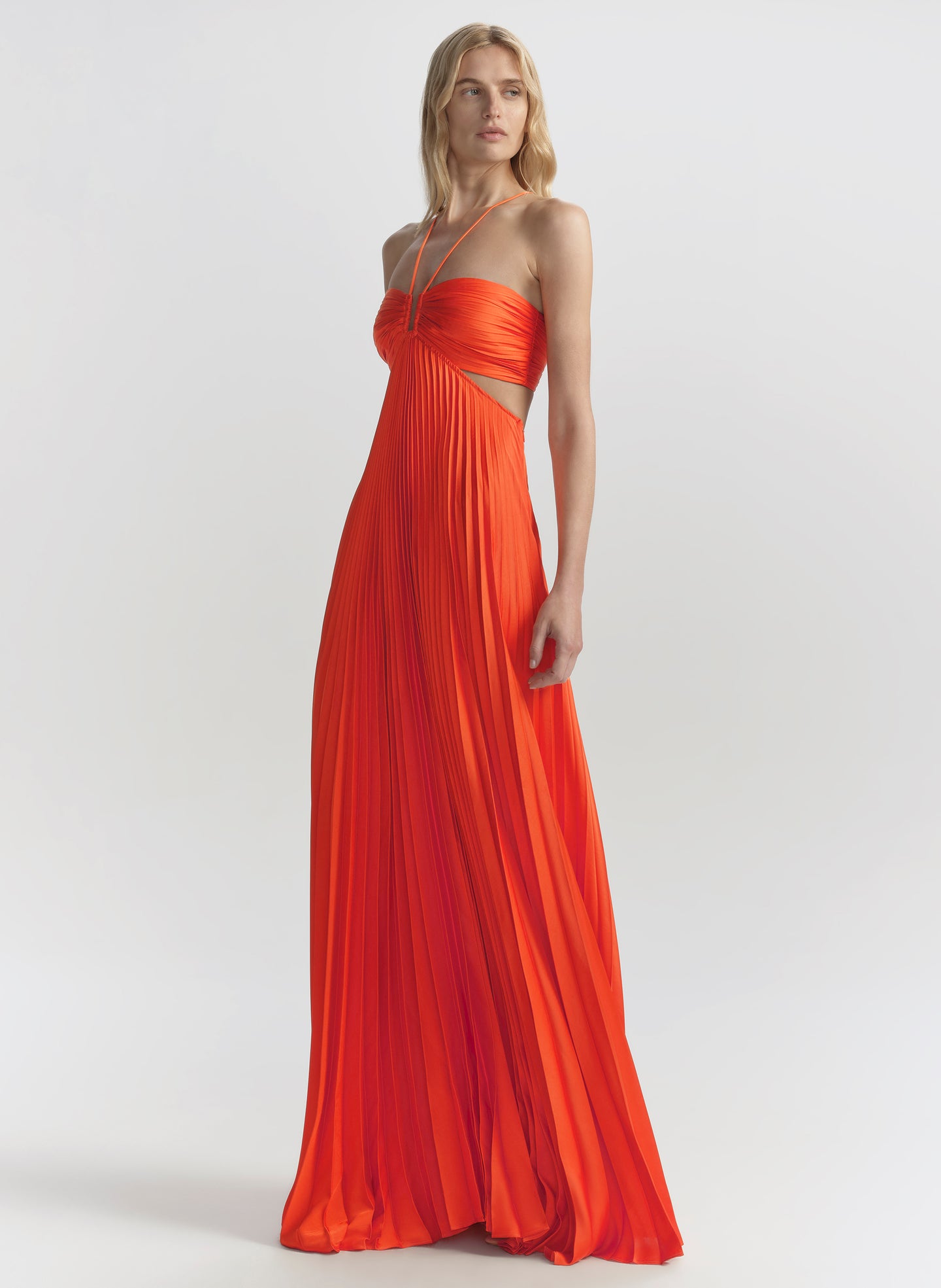 Woman wearing a long orange dress with cut-out design on a white background