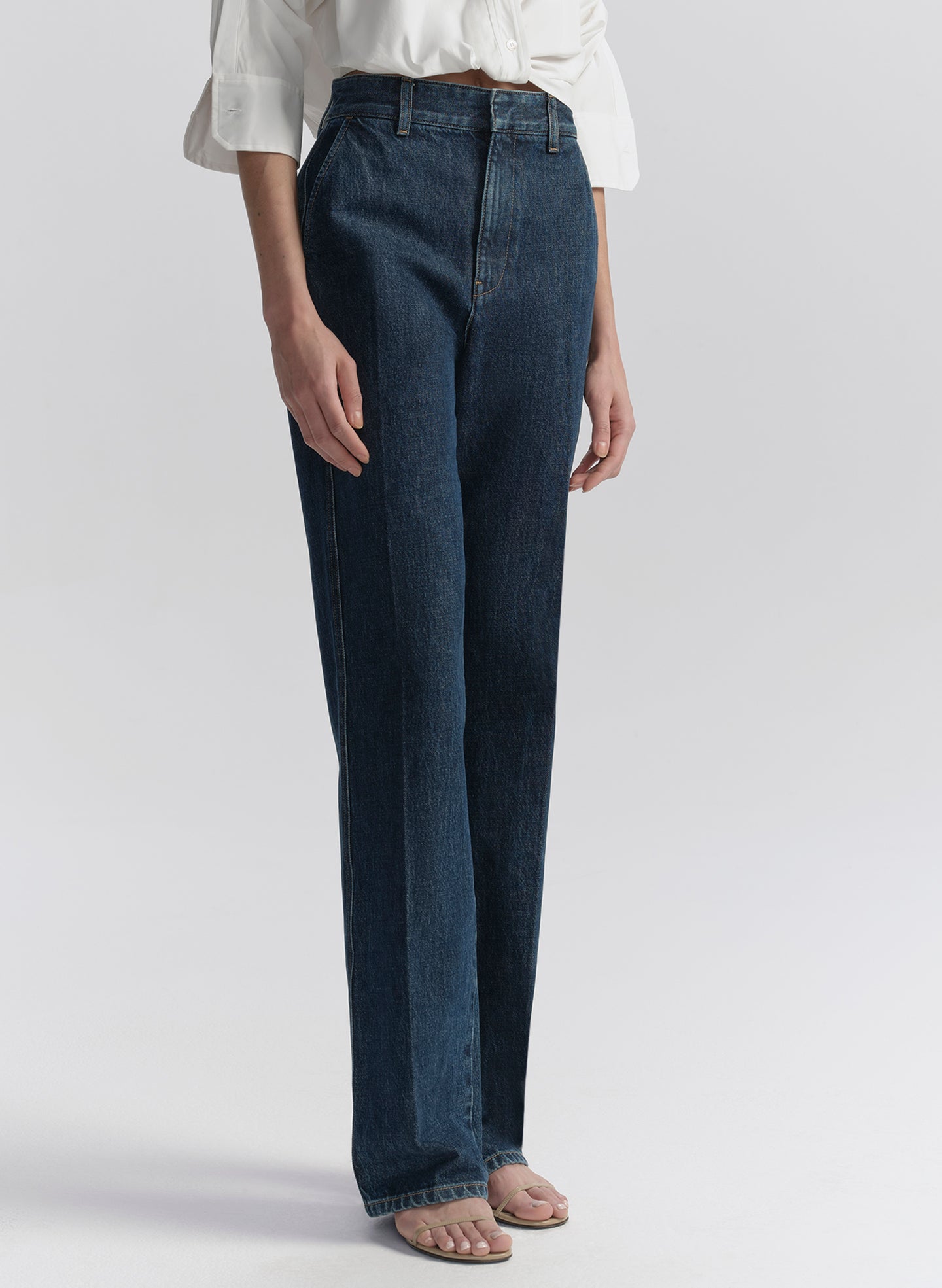 Person wearing dark blue jeans and a white shirt on a light gray background