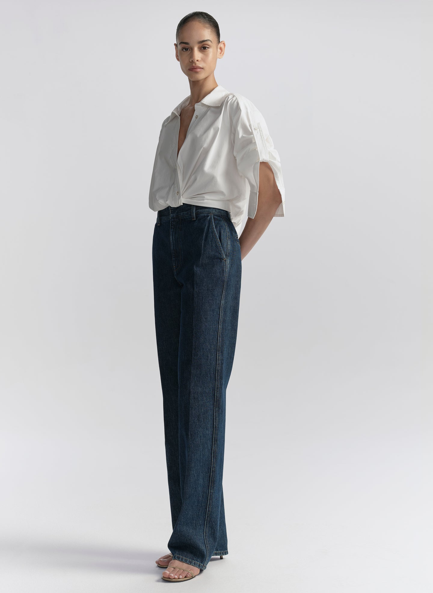 Person wearing a white shirt and dark blue jeans on a light gray background