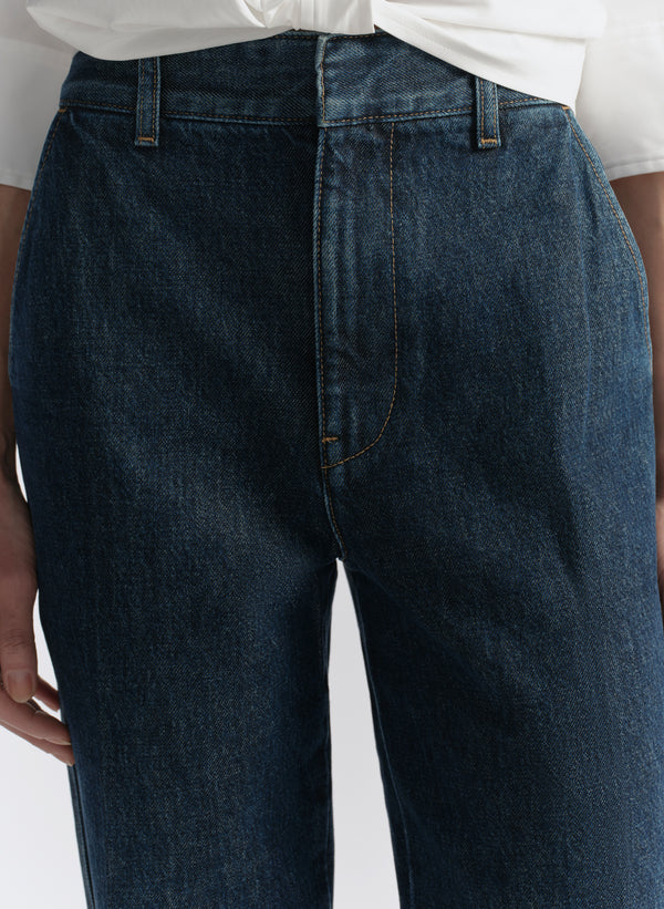 Dark blue jeans worn by a person on a light gray background