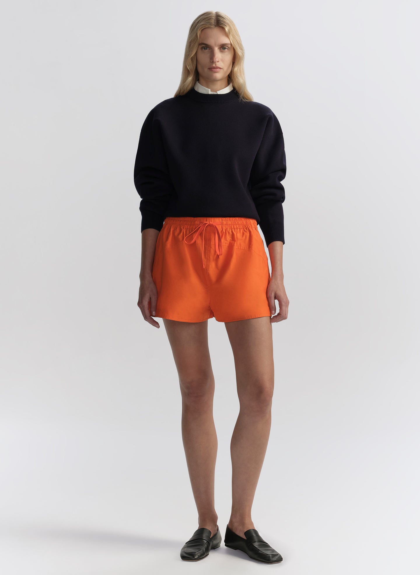 woman wearing a navy blue sweater and orange shorts on a white background