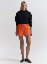 woman wearing a navy blue sweater and orange shorts on a white background