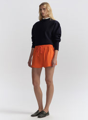 woman wearing a navy blue sweater and orange shorts on a white background