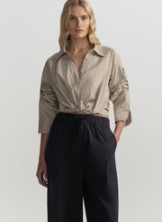 Woman wearing a beige shirt and black pants on a light gray background