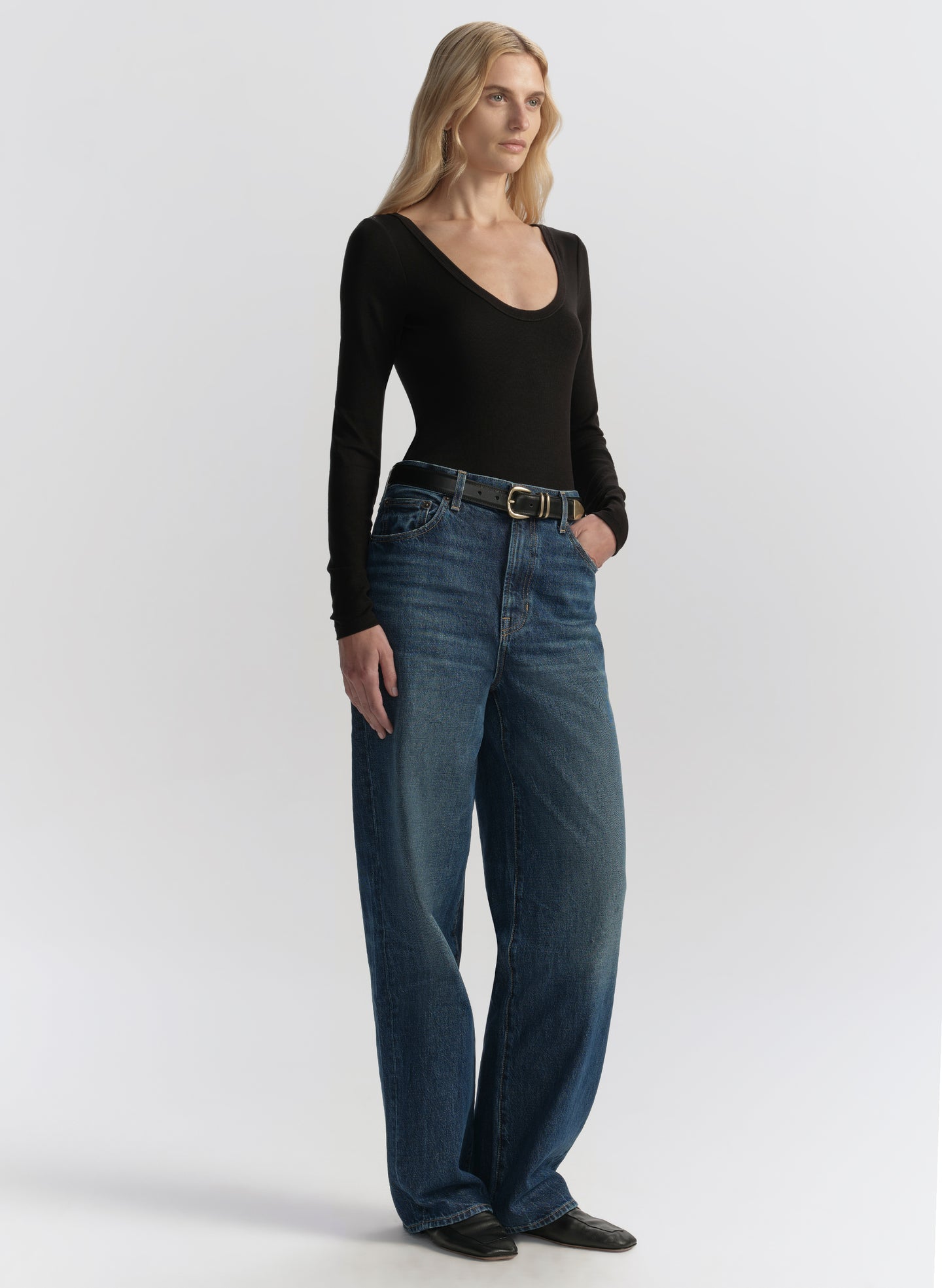 Woman wearing blue jeans and a black top on a white background