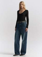 Woman wearing a black long-sleeve top and blue jeans on a white background