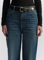 Person wearing blue jeans with a gold belt buckle on a white background