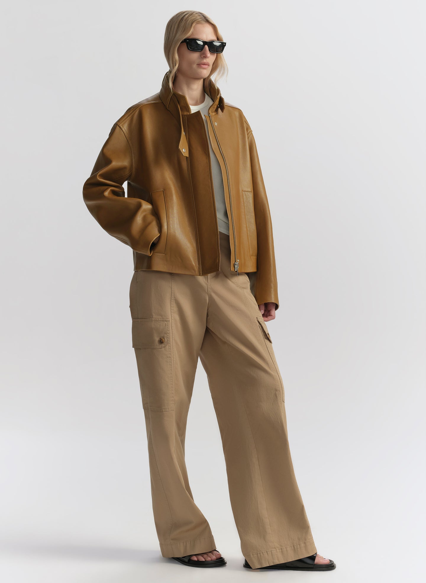 Person wearing a brown jacket and beige pants on a white background