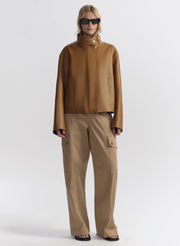 Person wearing a brown jacket and beige pants on a white background