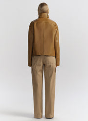 Person wearing a brown leather jacket and beige pants on a white background