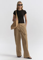 Woman wearing beige cargo pants and a black top, holding a beige bag on a white background
