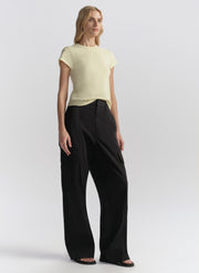 Woman wearing a light yellow top and blue pants on a white background