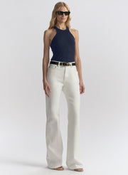 A model wearing a navy blue tank top, off-white wide-leg jeans with a black belt, and black sunglasses, standing against a light gray studio background.