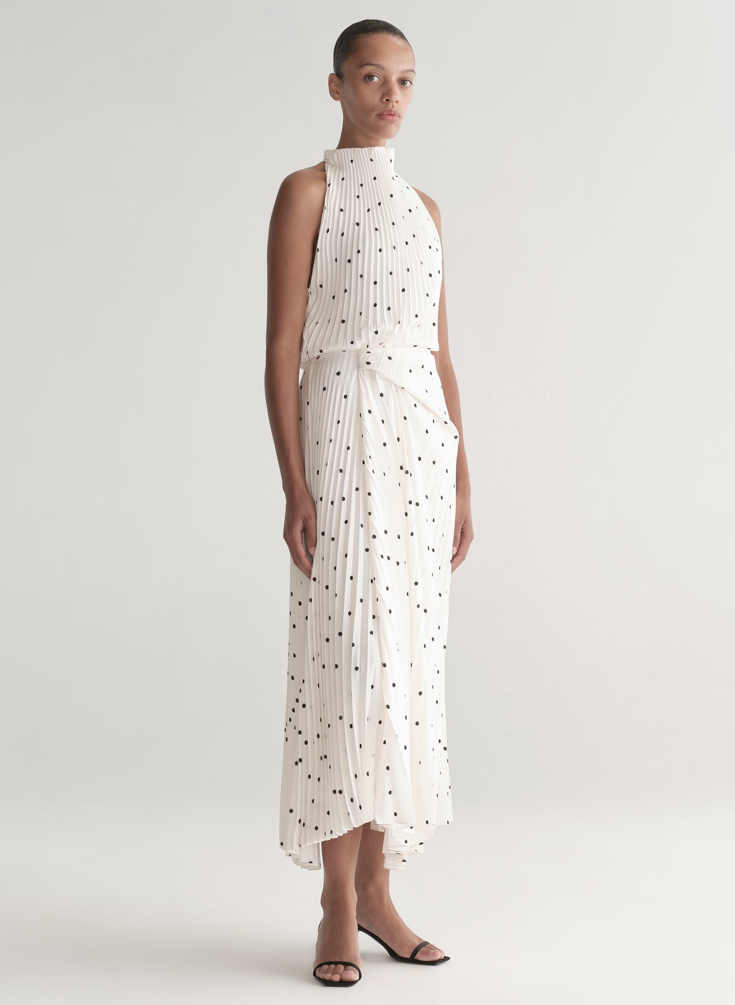 Woman wearing a white dress with black polka dots on a plain background