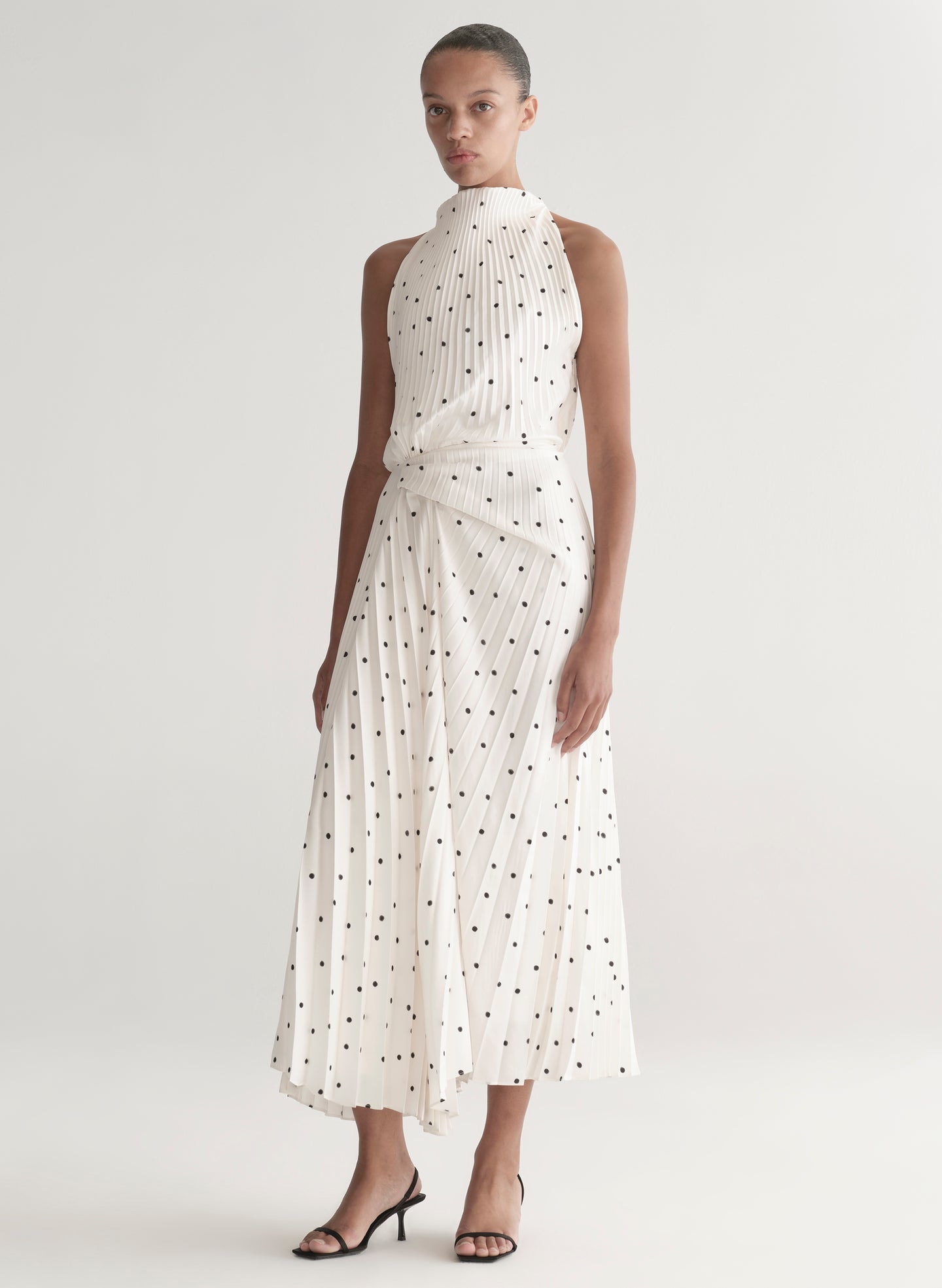 Woman wearing a white dress with black polka dots on a plain background