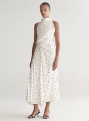 Woman wearing a white dress with black polka dots on a plain background