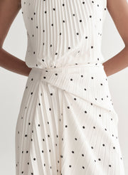 Woman wearing a white dress with black polka dots on a plain background
