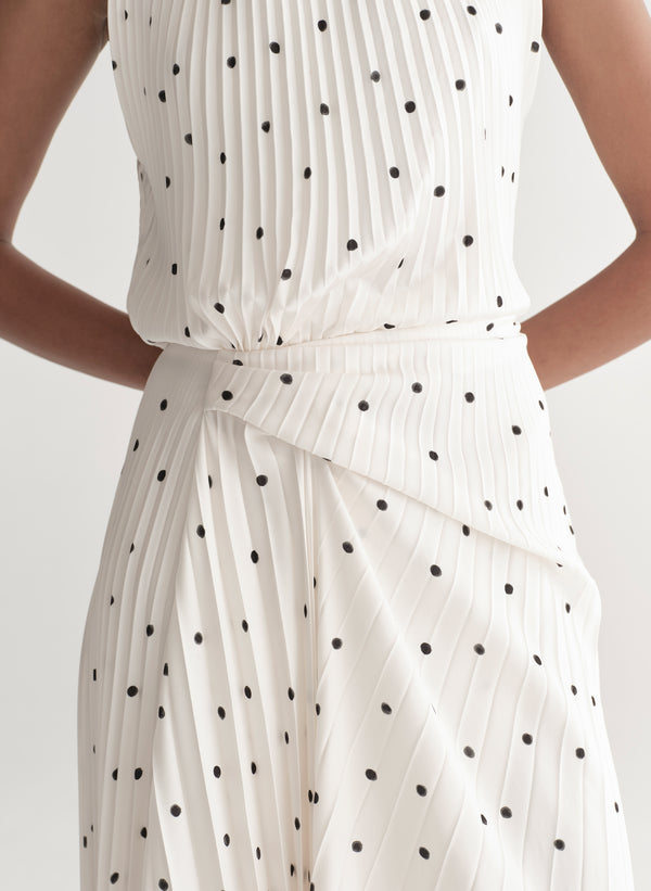 Woman wearing a white dress with black polka dots on a plain background