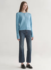 Woman wearing a light blue cardigan and dark jeans on a plain background