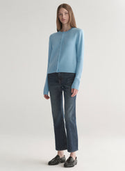 Woman wearing a light blue cardigan and dark jeans on a plain background