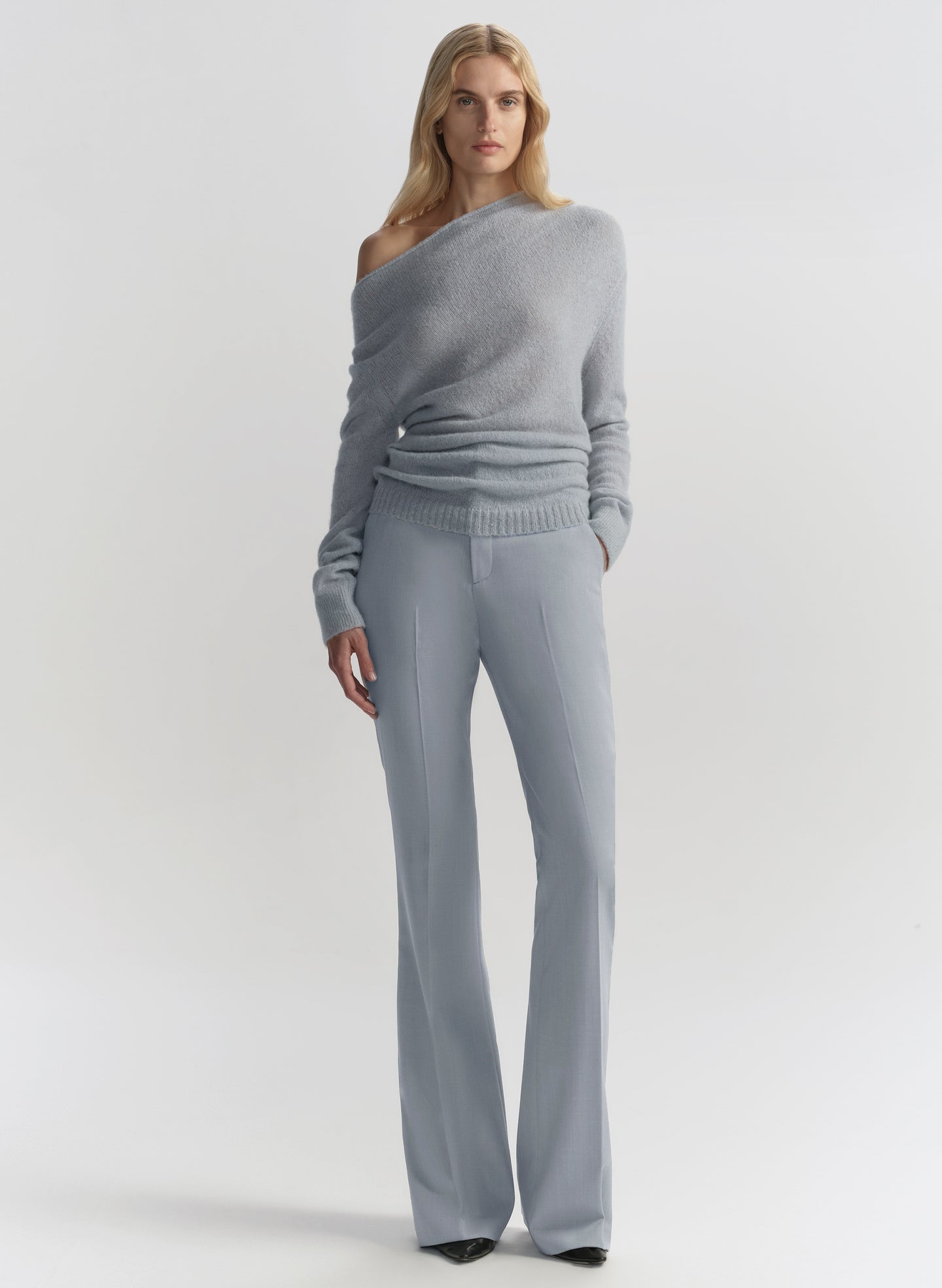 Woman wearing a gray off-shoulder sweater and matching pants on a light gray background
