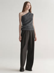 Woman wearing a gray one-shoulder top and dark grey pants on a plain background