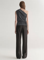 Woman wearing a gray one-shoulder top and dark grey pants on a plain background