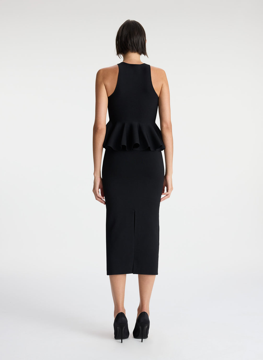 back  view of woman wearing black sleeveless peplum top and black midi skirt