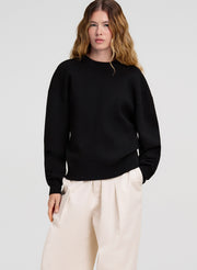 Person wearing a black sweater and white pants on a light gray background