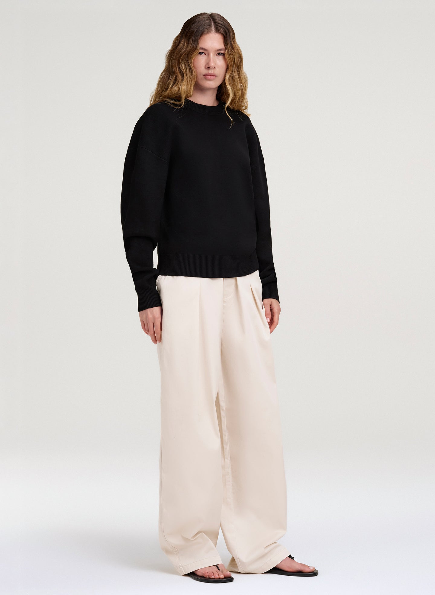 Person wearing a black sweater and white pants on a white background