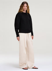 Person wearing a black sweater and white pants on a white background