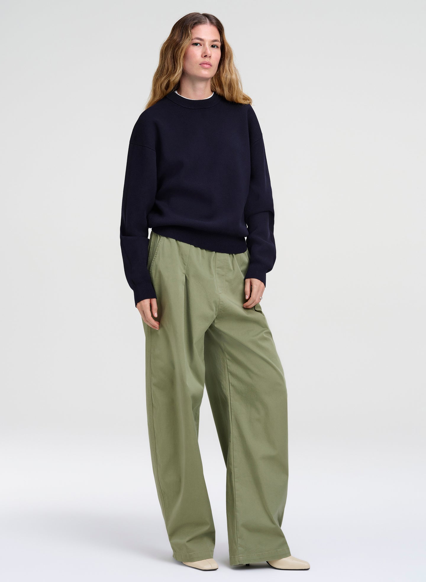 Person wearing a navy sweater and green pants on a white background
