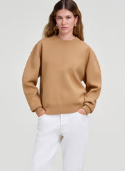 Woman wearing a brown sweater and white pants on a light background