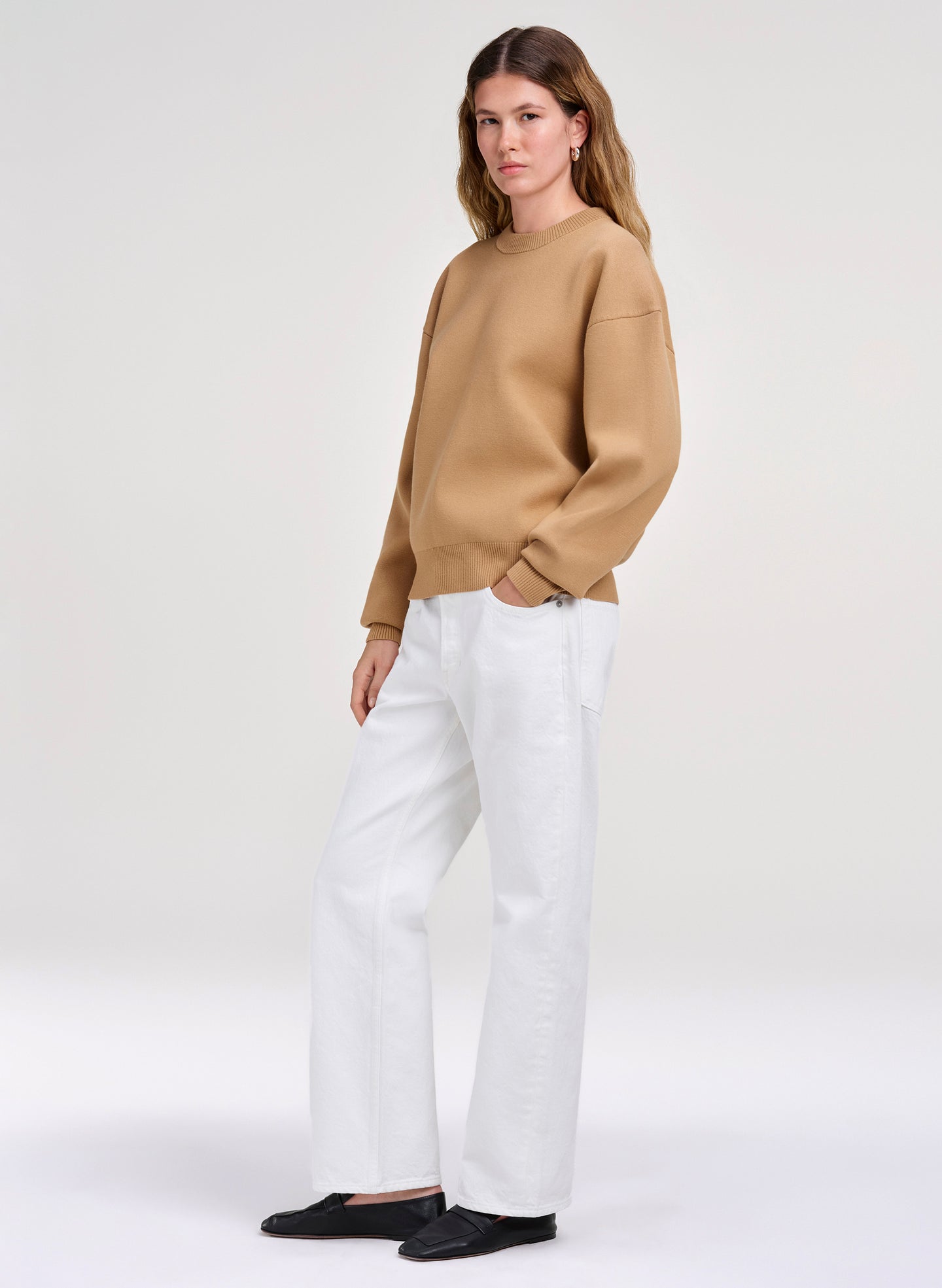 Woman wearing a beige sweater and white pants on a white background