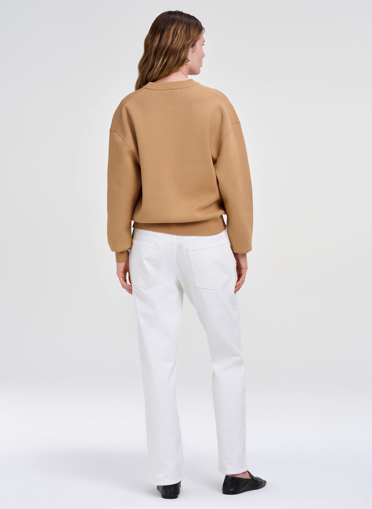 Person wearing a brown sweater and white pants on a white background