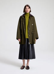 Person wearing a green coat, green sweater, and dark brown skirt on a white background