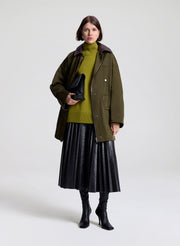 Person wearing a green coat, green sweater, and dark brown skirt on a white background