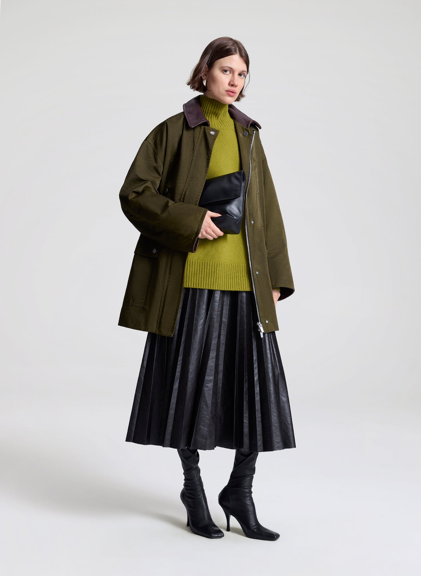 Person wearing a green coat, green sweater, and dark brown skirt on a white background