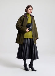 Person wearing a green coat, green sweater, and dark brown skirt on a white background