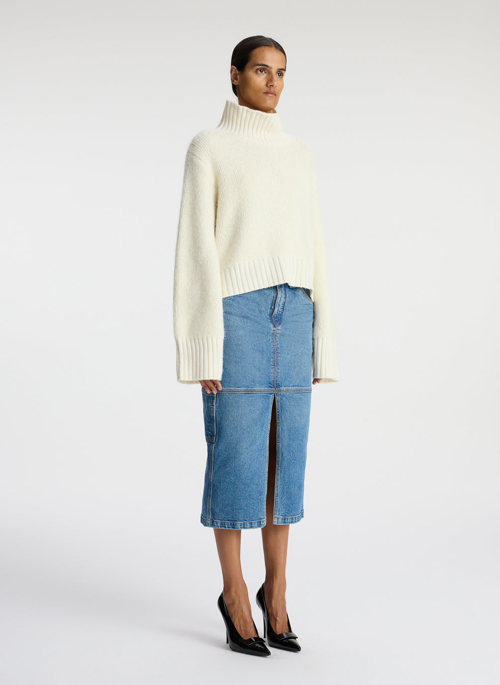 side view of woman wearing white turtleneck sweater and denim midi skirt
