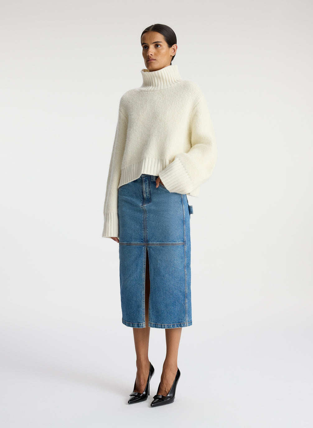 side view of woman wearing white turtleneck sweater and denim midi skirt