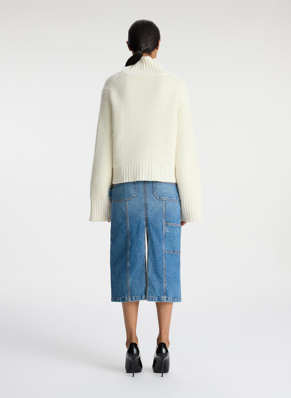 back view of woman wearing white turtleneck sweater and denim midi skirt